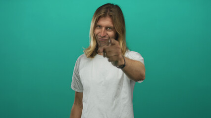 Fototapeta premium Blond man in white shirt with smug smile boldly points finger toward camera in green studio; confidence.