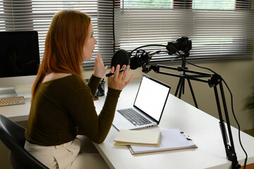 Side view of a female podcaster speaking into a podcast microphone while using a laptop during a...