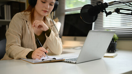 Cropped image of a woman recording an interview for a radio talk show using a microphone, laptop, and headphones in a modern home studio