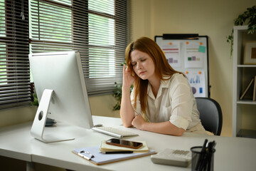 Serious Caucasian businesswoman experiencing stress while managing tasks on computer