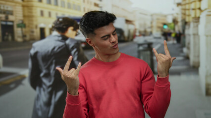 Young man wearing red sweater smiling and gesturing enthusiastically on a bustling city street during daylight.