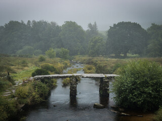 Postbridge Clapper Bridge over the East Dart River on a foggy and rainy day in Darmoor national park, Devon, England.