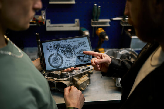 Mechanics discussing motorcycle repair using tablet in workshop