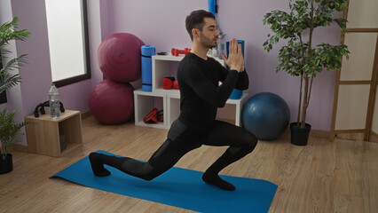 Young man performing yoga in a gym with fitness equipment around, showcasing focus and balance.