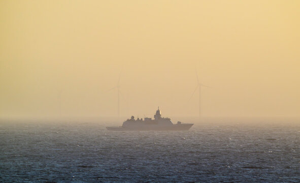 Dutch navy ship patrolling near offshore windfarm on misty North Sea
