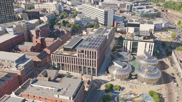 Aerial sunny flyover toward newly built Sheffield Hallam University campus, showcasing domes and cityscape.