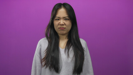 Woman expressing disgust with hands up and face crinkled against a vivid pink background, wearing a...