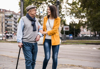 Elderly person and young adult walking together in the city smiling