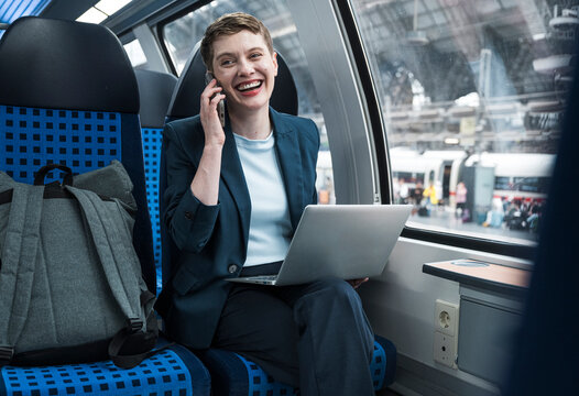 Smiling businesswoman with laptop and phone on train in station
