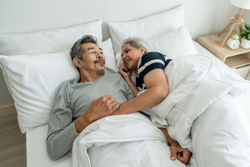 Asian elderly older couple lying down on bed, talking to each other. 