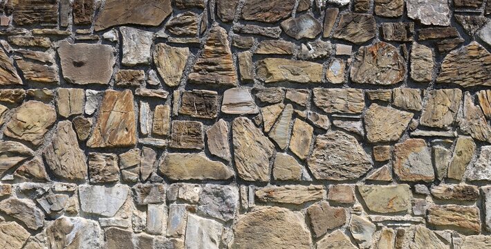 Massive stone wall with large brown and gray natural rocks. Background and texture