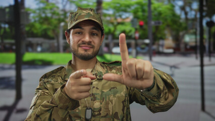 Man in camouflage uniform with visible dog tag points finger and frames view with an l shape hand...