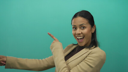 Smiling hispanic woman in beige pointing energetically against a vibrant green background, expressing excitement and positivity.