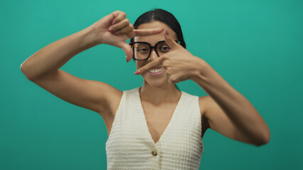 Woman with glasses framing with fingers against isolated green background wall smiling confidently...