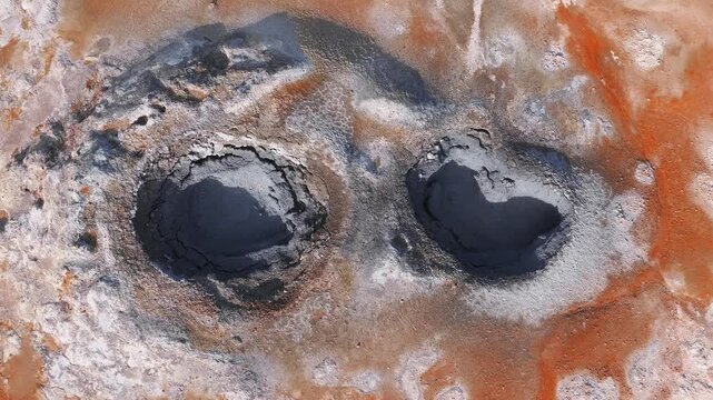 Aerial view of Hverir geothermal area in Iceland, showing orange and white mineral deposits and dynamic bubbling mud pools with ripples and splashes.