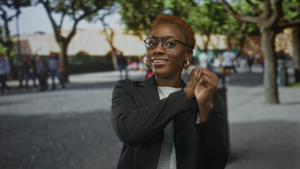 Young african american woman pointing both thumbs backward on urban street with stone pavement and...