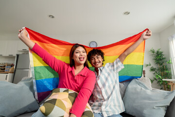 Portrait of transgender woman and partner holding rainbow flag in house. 