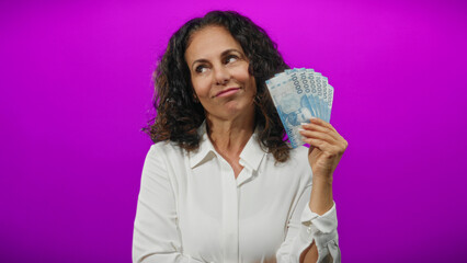 Middle-aged woman holding chilean pesos against a vivid purple wall, emphasizing currency and...