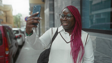 Woman with pink braids making a video call on a city street with cars in the background, using...