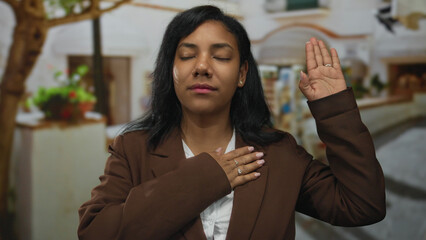 Woman with hand on chest and raised hand standing on a cobblestone street under warm sunlight...