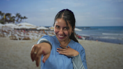Young hispanic woman in blue attire laughing and enjoying a sunny day at the beach, with palm trees...