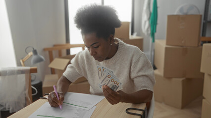 Woman reviewing finance documents with dollar bills in hand surrounded by moving boxes in a new...