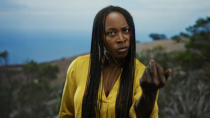 Woman with braids wearing yellow shirt at seaside pointing with intense expression against ocean...