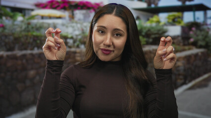 Young hispanic woman holds both hands fingers in air quotes against a stone wall along an urban...