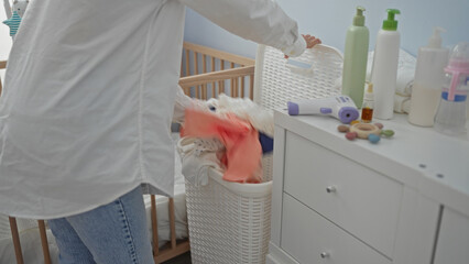 Woman in laundry room sorting clothes near changing table, surrounded by baby bottles, cleaning...