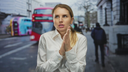 Woman standing on a city street rubbing hands for warmth with a red bus passing by in an urban...