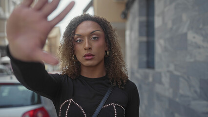 Woman holds out her hand in a stop gesture on a narrow urban street beside a stone building;...