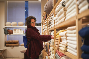 Woman shopping for cozy blankets in modern home goods store