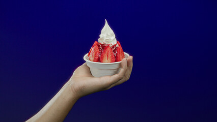 Caucasian man's hand holding strawberry sundae against bright blue background, showcasing isolated...