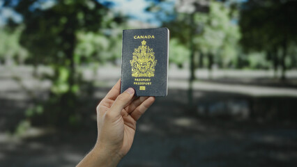 Man holding a canadian passport outdoors, highlighting travel in a park setting with a focus on...
