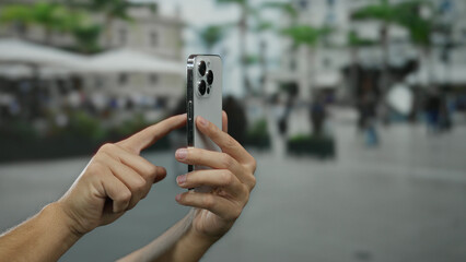 Fototapeta premium Man using smartphone outdoors on a city street with blurred background holding device in hand and tapping screen.