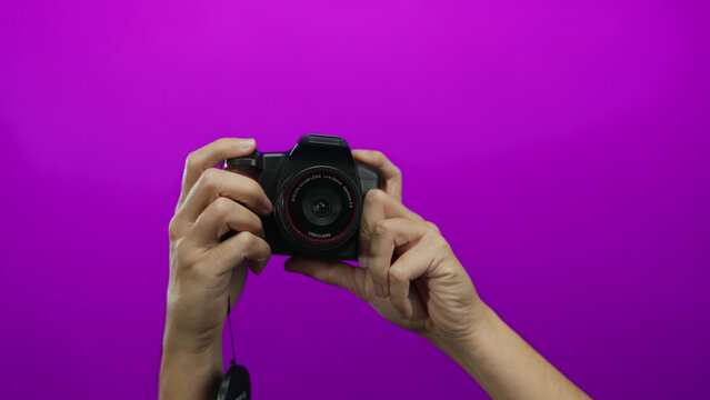 Caucasian man's hands holding a camera against a vibrant pink background, showcasing photography equipment and creativity in an isolated studio setting.