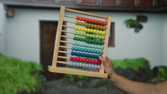 Man holding colorful abacus outside on a city street with a house in the background, showcasing vibrant beads against a suburban town setting.