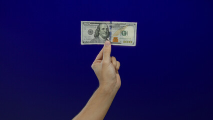 Caucasian man holding a united states hundred dollar bill against a vivid blue isolated background,...