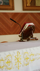 Pulpit with microphone and open bible on altar inside a church setting featuring ornate decorations and framed religious artwork in a serene indoor environment.