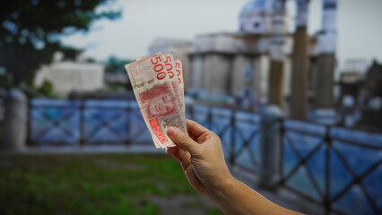 Hand holding swedish krona banknotes outdoors in an urban setting, symbolizing financial...