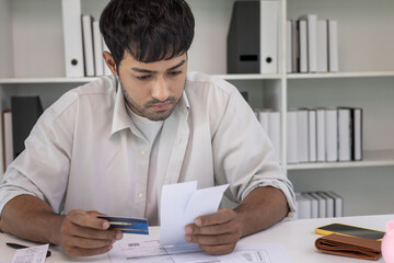 Stressed and headache asian man with large bills or invoices no money to pay to expenses and credit...