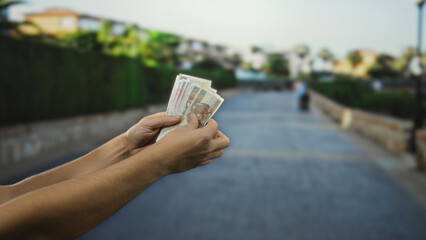 Man holding polish zloty banknotes outdoors on a city street, showcasing currency and finance in an urban setting with a clear sky backdrop.