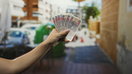 Man holding polish zloty banknotes near outdoor recycling bins surrounded by garbage and containers...