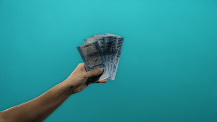 Male hand holding hungarian forint banknotes against a vivid blue background, symbolizing financial...