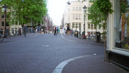 Blurred scene of people walking on a cobblestone street in amsterdam, with bicycles and historic buildings creating a classic dutch city atmosphere in the background.