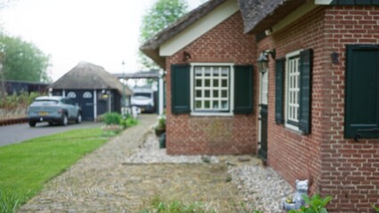 Blurred image of a traditional brick house front in the netherlands, featuring a bokeh effect with a car in the driveway and garden pathway.