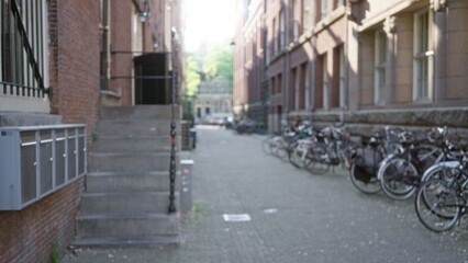 Defocused view of a charming european alleyway lined with bicycles, bordered by picturesque historical buildings, evoking a tranquil city atmosphere bathed in soft sunlight.