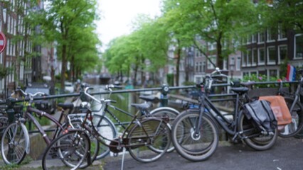 Bicycles parked alongside the picturesque canals in amsterdam with blurred, lush greenery and historic architecture forming a classic dutch background.