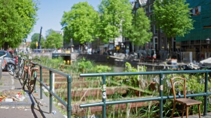 Obraz premium Bicycle resting by amsterdam canal with blurred bokeh background, showcasing iconic green trees and traditional architecture in the netherlands.