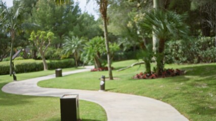 Blurred path through a lush tropical resort showcasing vibrant green palms and colorful floral...